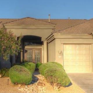 A single-story house with a garage and desert landscaping in the front yard.