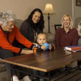 A joyful moment captured with four generations together, enjoying time in a cozy living room.