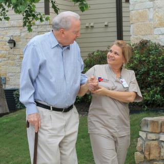 An elderly person receiving support from a caregiver while walking outside.