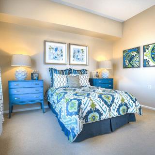 A modern bedroom with blue-toned decor, featuring patterned bedding and wall art.