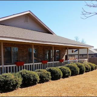 A charming house with a spacious porch and well-maintained landscaping under a clear blue sky.