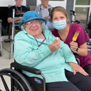 A caregiver and an elderly woman enjoy a cheerful moment outdoors, showcasing the joy of companionship.
