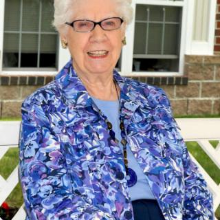 A cheerful elderly woman in a vibrant blue floral jacket, enjoying a sunny day outdoors.