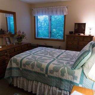 A cozy bedroom with a neatly made bed, wooden furniture, and a window view.