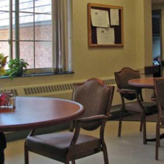 An empty cafeteria with round tables and chairs near a window and bulletin board.