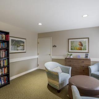 A cozy office space featuring a bookshelf, comfortable chairs, and wall art.