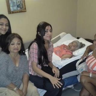 A family gathered around an elderly person in a bedroom setting.