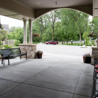 A view from a covered porch overlooking a driveway and lush greenery.
