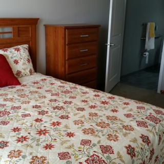 A cozy bedroom featuring a bed with floral bedding and a wooden dresser.