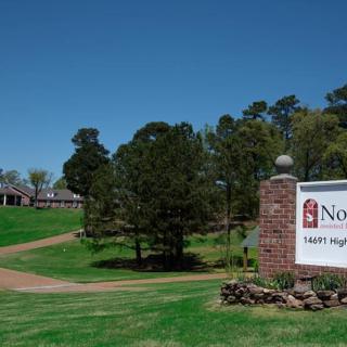 A school entrance with a sign displaying the school's name, surrounded by greenery and trees.