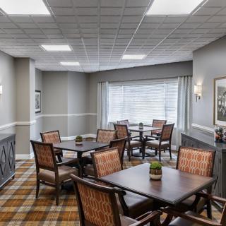 A cozy dining area with multiple tables and chairs, featuring large windows and ceiling lighting.
