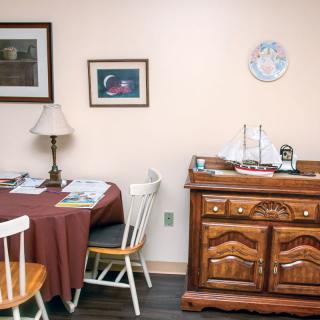 A cozy dining area with a round table, chairs, lamp, and decorative cabinet.