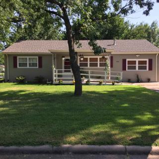 A suburban house with a front porch, surrounded by a well-maintained lawn and a large tree in the front yard.