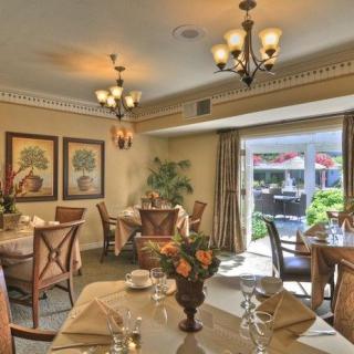 An elegantly furnished dining room with chandeliers and neatly set tables, overlooking a garden through large windows.