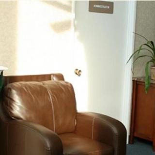 A cozy office space with a leather chair and a potted plant by the door, lit by natural sunlight.