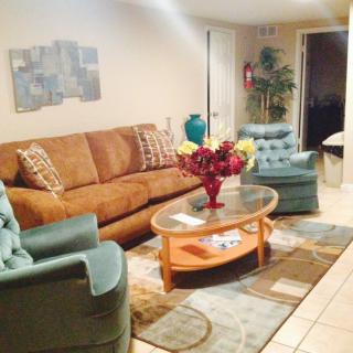 A cozy living room with a brown sofa, two blue armchairs, and a glass coffee table decorated with flowers.