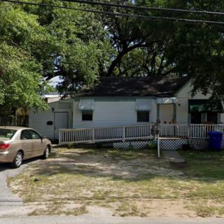 A small house with a driveway and a car parked under surrounding trees.