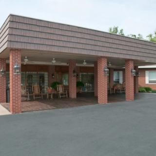 A brick building with a covered entrance and columns, featuring a paved driveway.