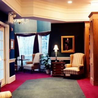A cozy and elegant lobby area featuring armchairs, a side table with a lamp, and a framed painting on the wall.