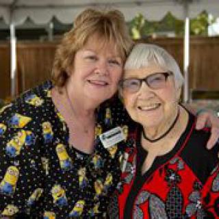 Two women smiling and embracing each other outdoors.