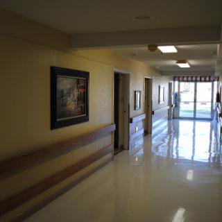 A well-lit hospital hallway featuring doors to patient rooms and framed artwork on the walls.