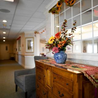 A warmly decorated hallway featuring a wooden dresser with a vase of colorful flowers.