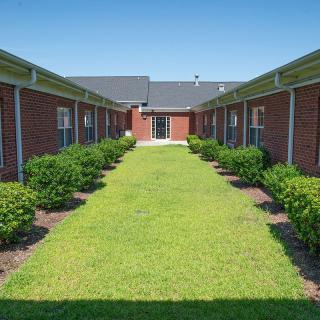 A neatly landscaped courtyard between brick buildings, featuring a grassy area flanked by bushes.
