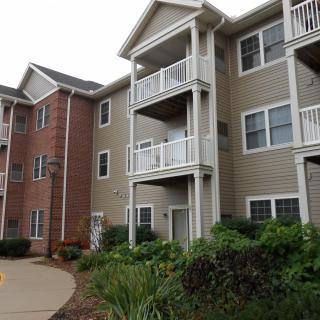 A residential apartment building with balconies, featuring a combination of brick and siding exterior.