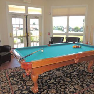 A well-lit game room with a pool table and comfortable chairs by the windows.