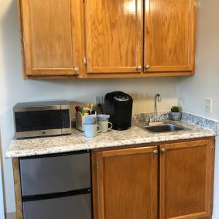 A compact kitchen setup featuring wooden cabinets, a microwave, coffee maker, and a small refrigerator.