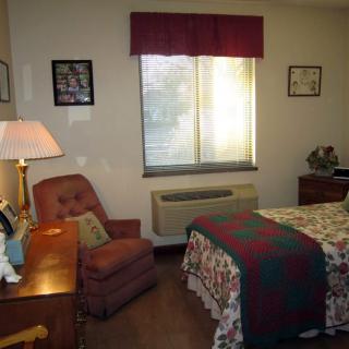 A cozy bedroom with a bed, armchair, and window featuring classic decor.