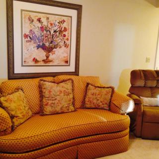 A cozy living room with a patterned sofa, recliner, and floral artwork hanging on the wall.