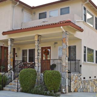 A two-story residential house with a front porch featuring stone columns and manicured shrubs.