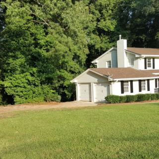 A suburban house surrounded by trees and a well-maintained lawn.