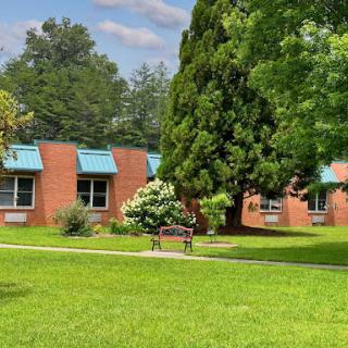 A serene view of a school building surrounded by lush greenery and a clear blue sky.