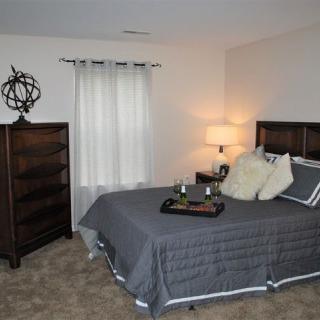 A cozy bedroom interior with a neatly made bed, decorative pillows, and a bedside lamp.