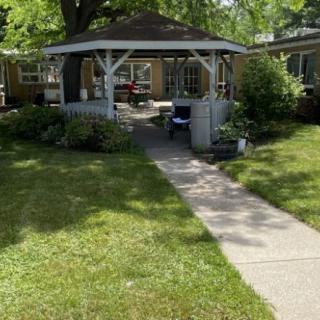 A cozy gazebo nestled in a lush green yard with a concrete pathway leading to it.