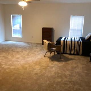 A spacious bedroom with minimal furniture and carpeted flooring.