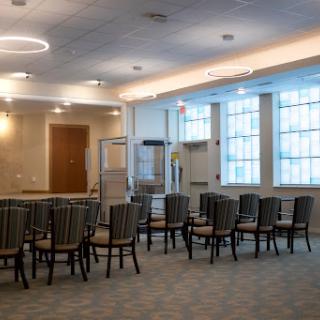 A spacious interior room featuring arranged chairs, modern lighting, and large windows.