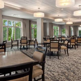 A well-lit dining area with neatly arranged tables and chairs, featuring large windows and modern lighting.