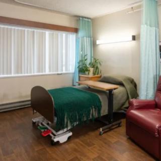 A hospital room with a bed, a red armchair, and a small table next to the window.