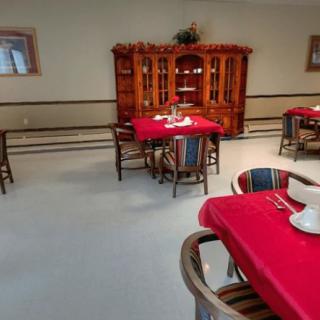 A cozy dining room setup with tables covered in red tablecloths and a wooden cabinet against the wall.