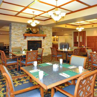 A cozy dining area with tables and chairs, featuring a fireplace and elegant chandeliers.