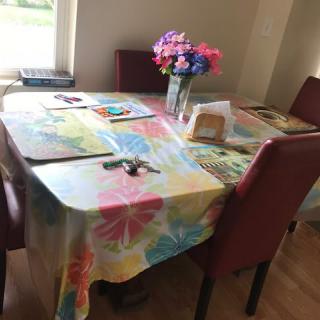 A dining table with a colorful tablecloth, adorned with flowers and surrounded by chairs.