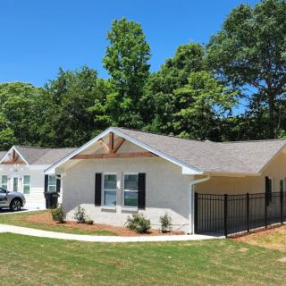 A suburban residential house with a well-maintained yard and surrounding trees under a clear blue sky.