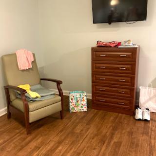 A cozy room featuring a comfortable chair, a dresser, and a television mounted on the wall.