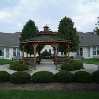 A wooden gazebo in a landscaped garden setting with neatly trimmed bushes.