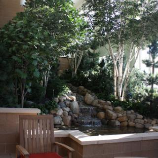 A serene indoor garden featuring a tranquil waterfall surrounded by lush greenery and a comfortable wooden chair.