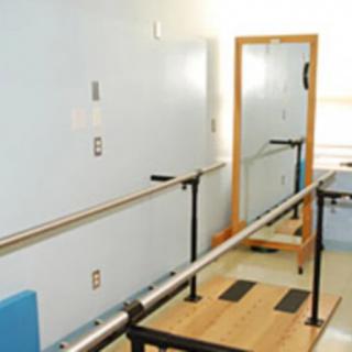 A physical therapy room featuring parallel bars and a mirror for rehabilitation exercises.