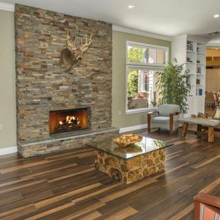 A cozy living room with a stone fireplace, warm wood flooring, and modern decor.